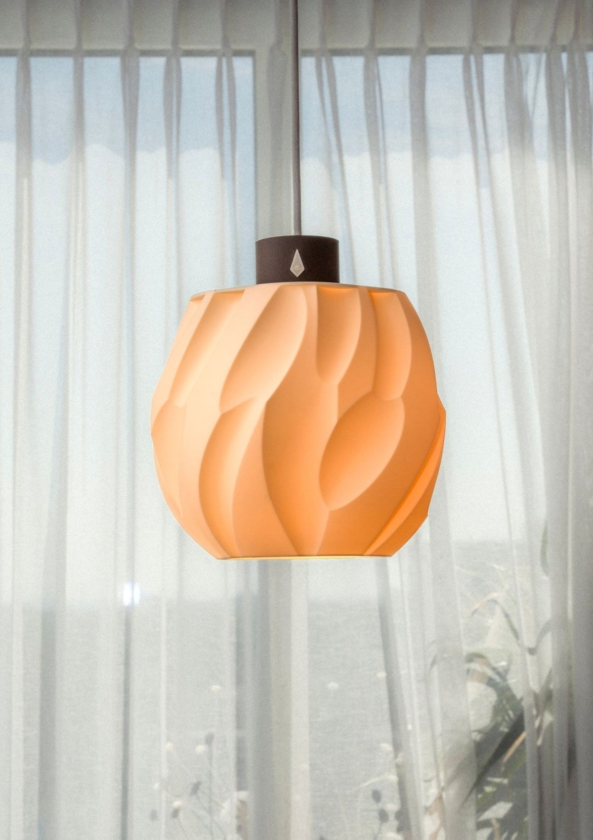 Bolvormige hanglamp met diep zandreliëf en warm brandend licht voor een raam met wit gordijn.