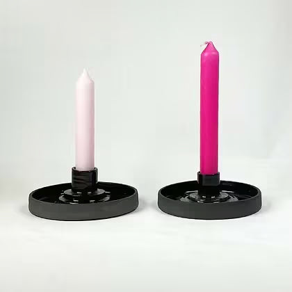 Twee vlakke zwarte keramieken kandelaars met een roze en een felroze dinerkaars.