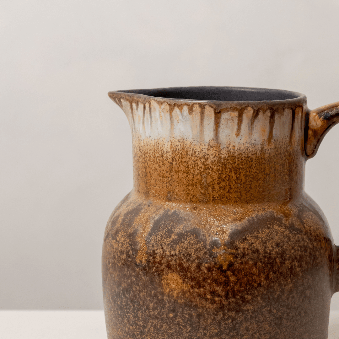 Close-up van de hals: crème glazuur dat overloopt in amber en donkerbruine spikkels.