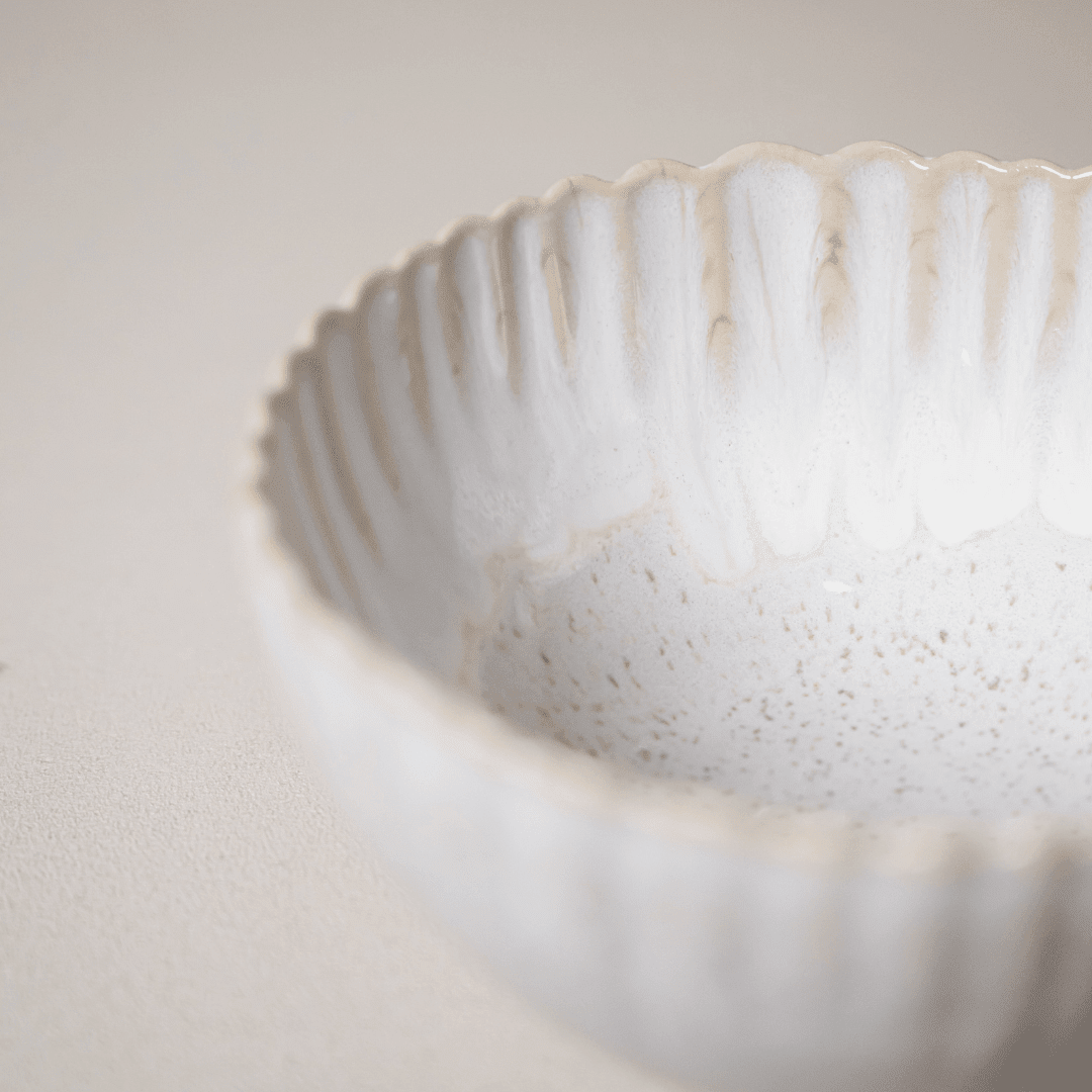 Close-up van de geribbelde geschulpte rand van een gebroken witte kom.