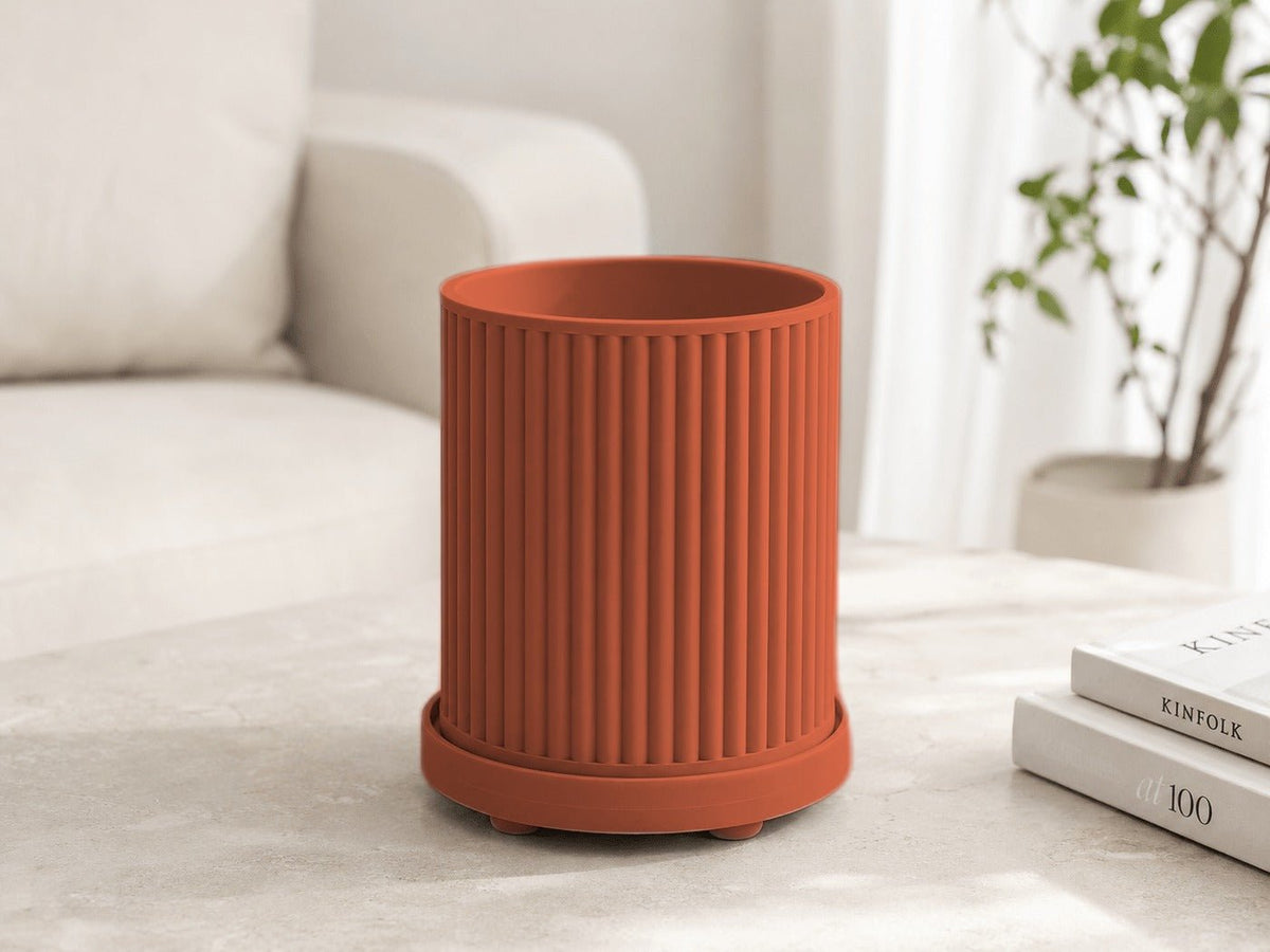 Geribbelde plantenpot in terracotta met onderschotel, op een tafel bij een bank.