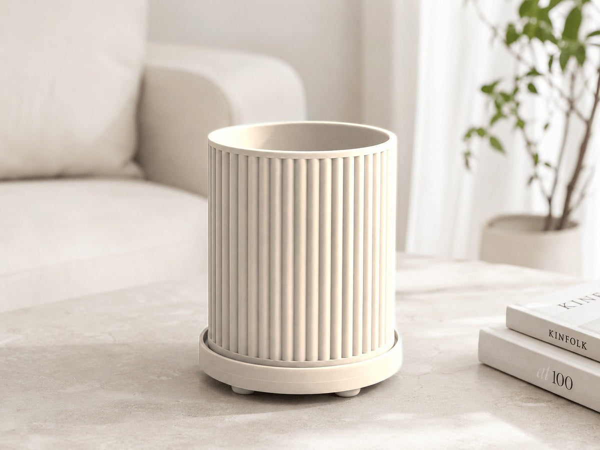 Geribbelde plantenpot in mat wit met onderschotel, op een tafel bij een bank.