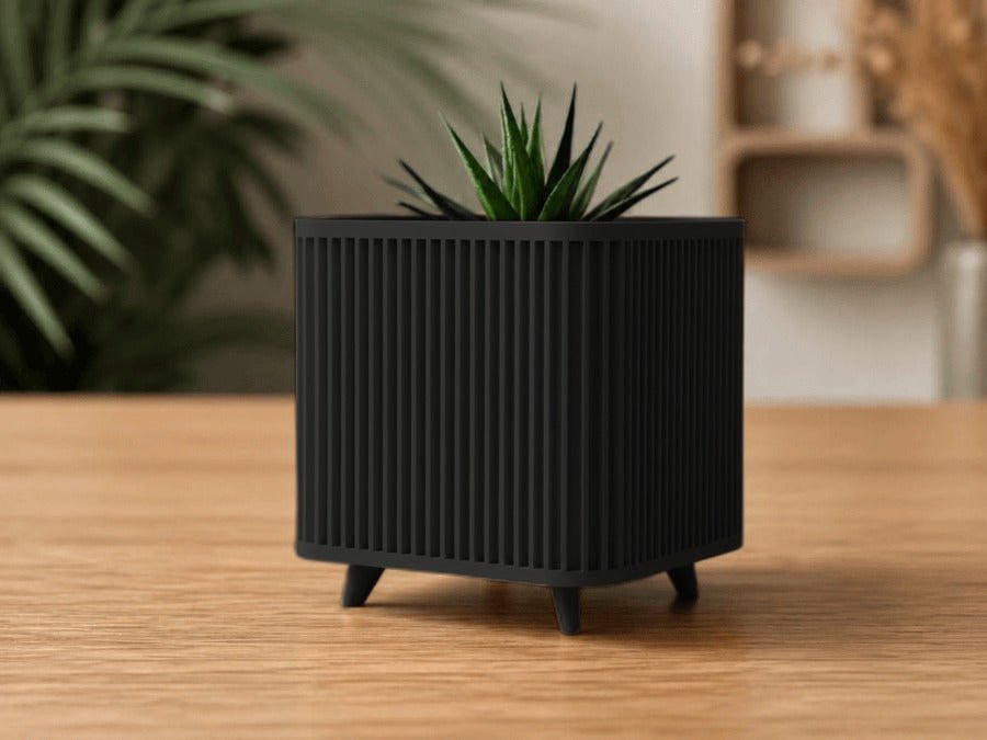 Vierkante plantenpot op pootjes in mat zwart met verticale ribbels, met een vetplant.