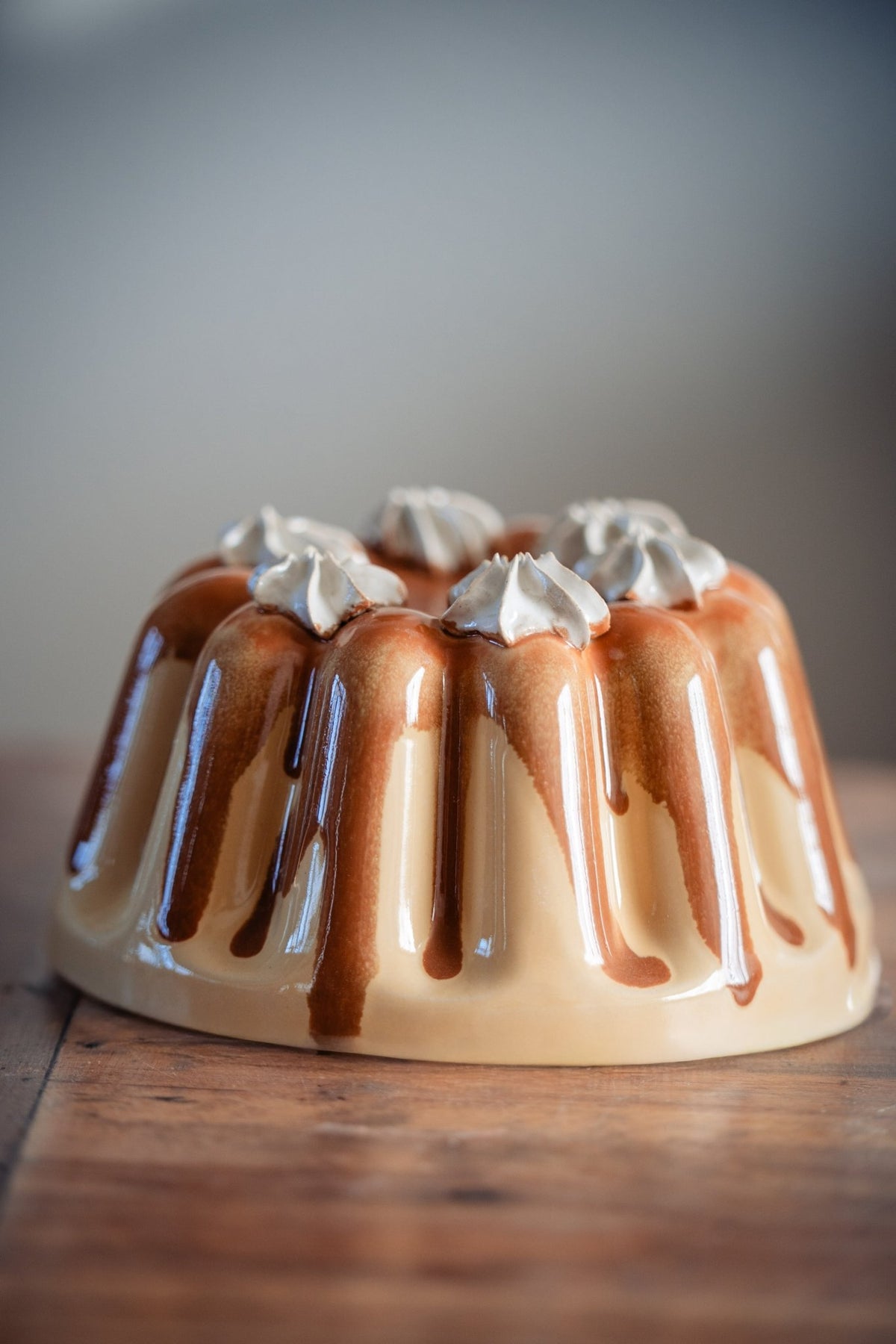 Keramieken puddingvorm met karamelkleurig glazuur en witte slagroomtoefjes op een houten tafel.