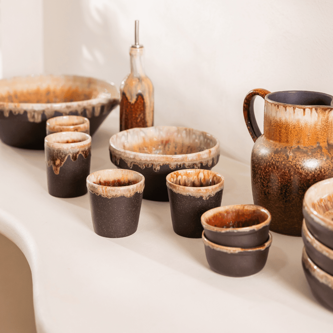 Servies in donkerbruin keramiek met druipglazuur op een lichte tafel.