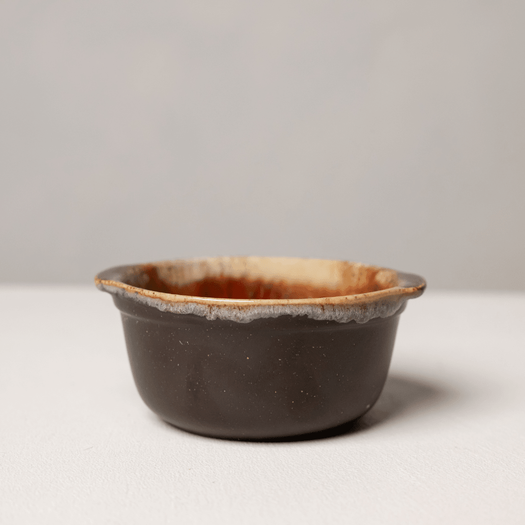 Klein donkerbruin keramieken schaaltje met crème glazuurrand, van opzij.