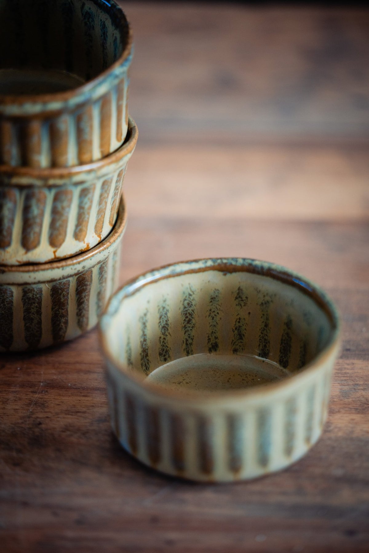 Gestapelde geribbelde keramieken schaaltjes met beige en groen glazuur.