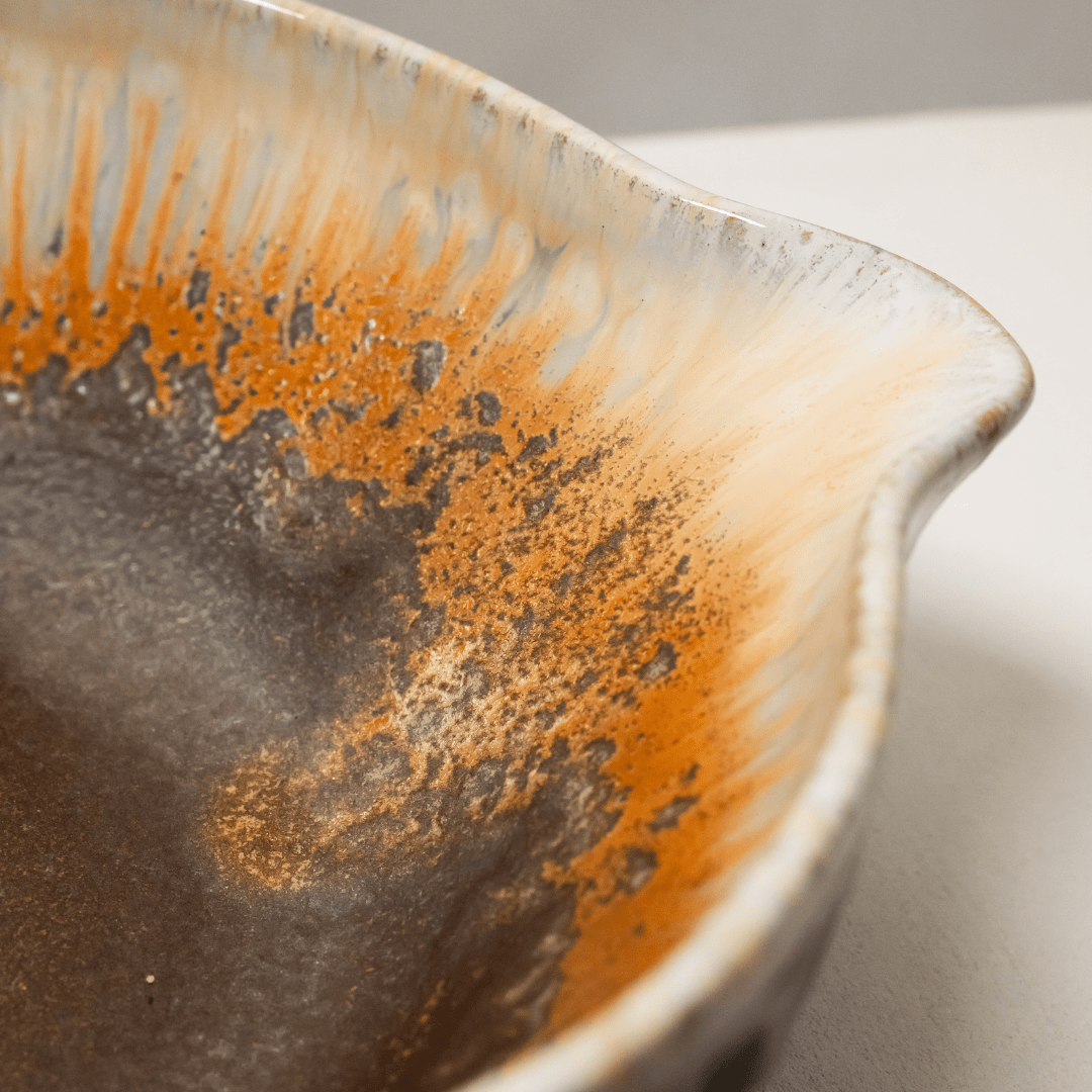 Close-up van het glazuur: oranje spikkels en crème strepen boven een grijsbruine bodem.