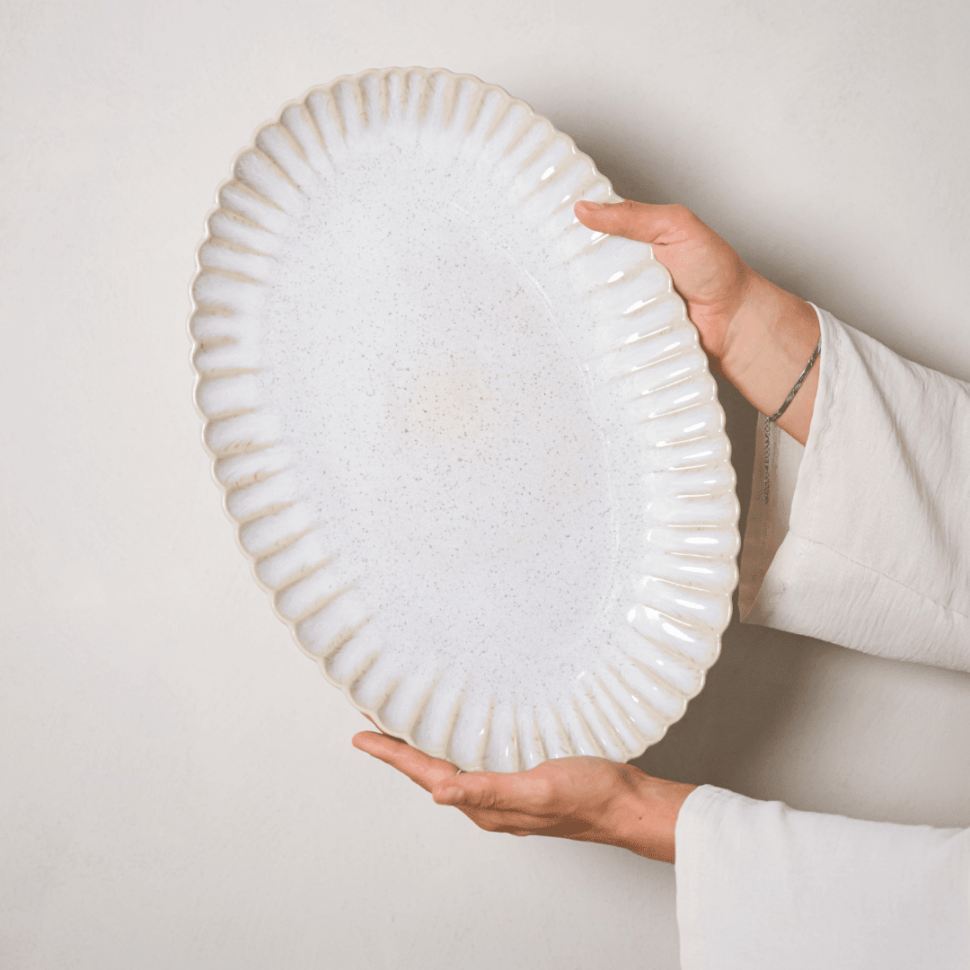 Ovale gebroken witte schaal met geschulpte rand, rechtop vastgehouden.