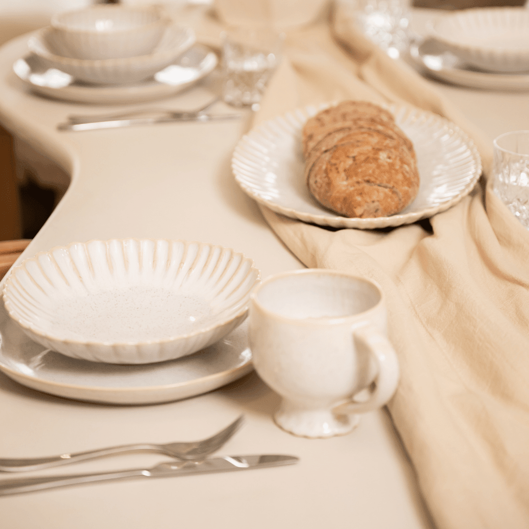 Gebroken wit servies op een linnen loper met brood, bestek en glazen.