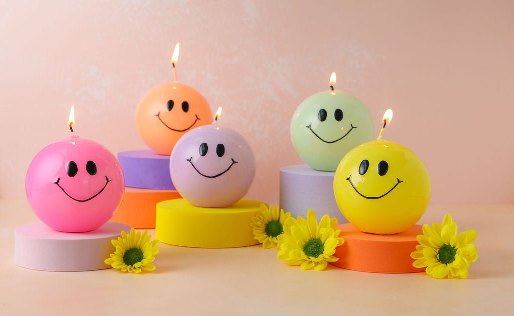 Een handgemaakte gele bolkaars rond met een zwart smiley gezicht erop.