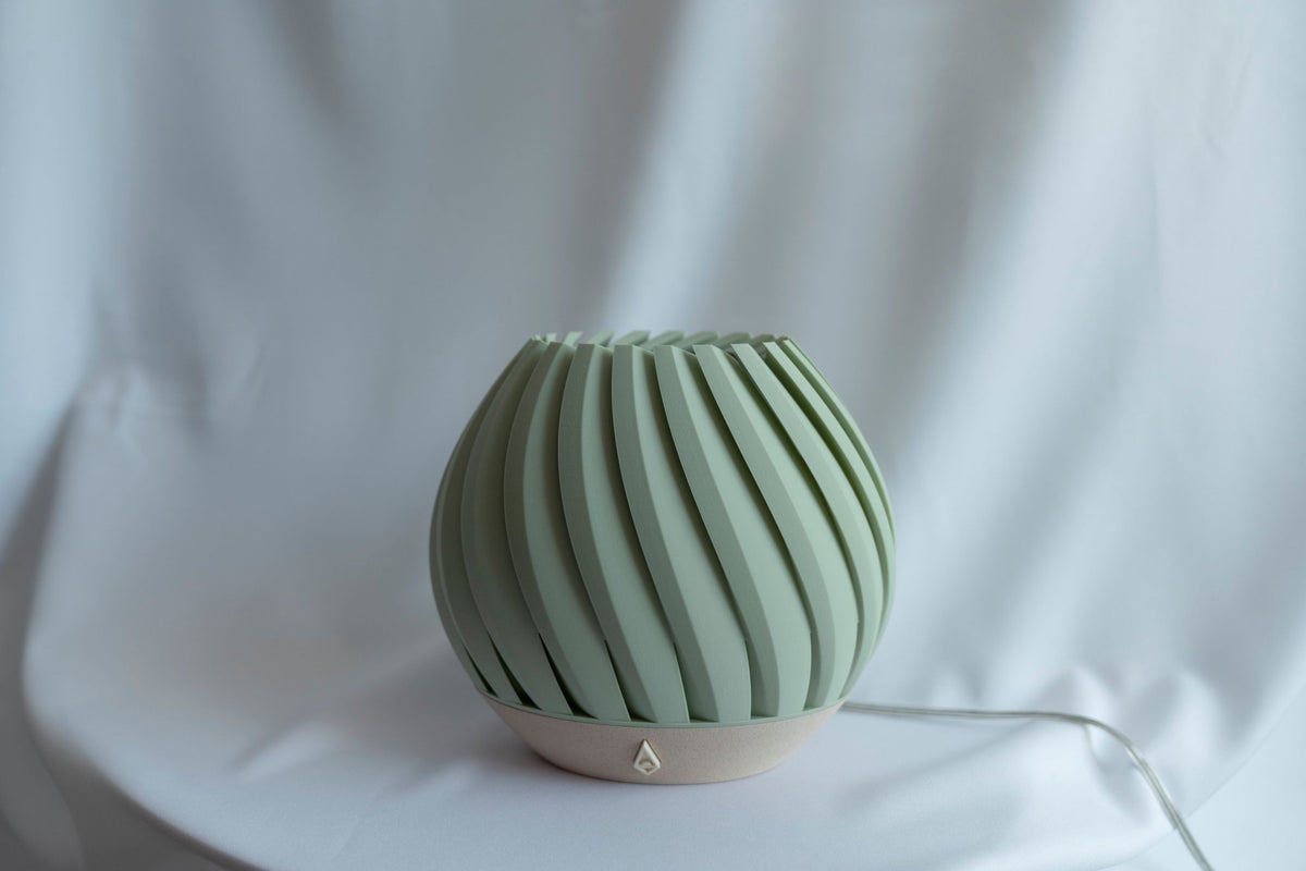 Zeegroene brede tafellamp met geribbelde schelpvorm tegen een witte doek, uitgeschakeld.