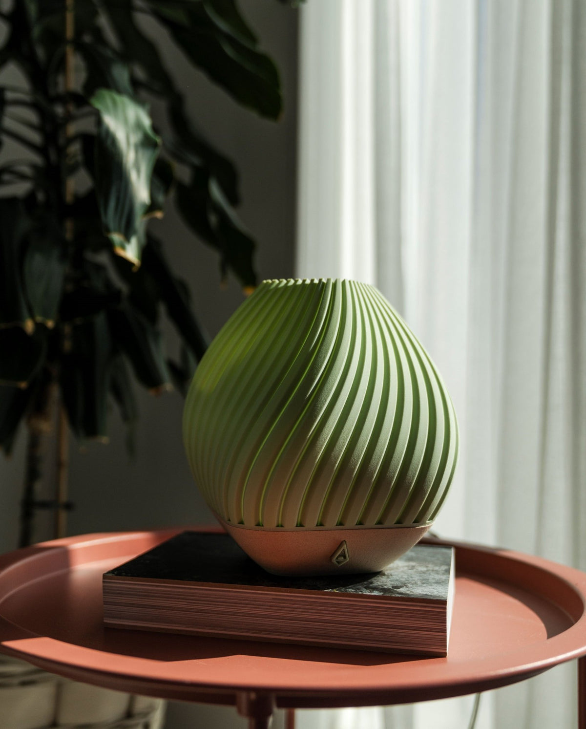 Groene geribbelde tafellamp met ronde schelpvorm op een roze bijzettafel, met planten op de achtergrond.