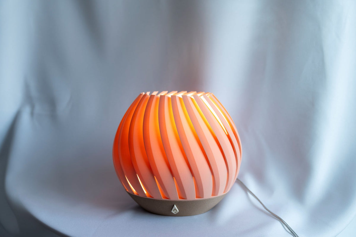 Koraalroze brede tafellamp met warm brandend licht tegen een witte doek.