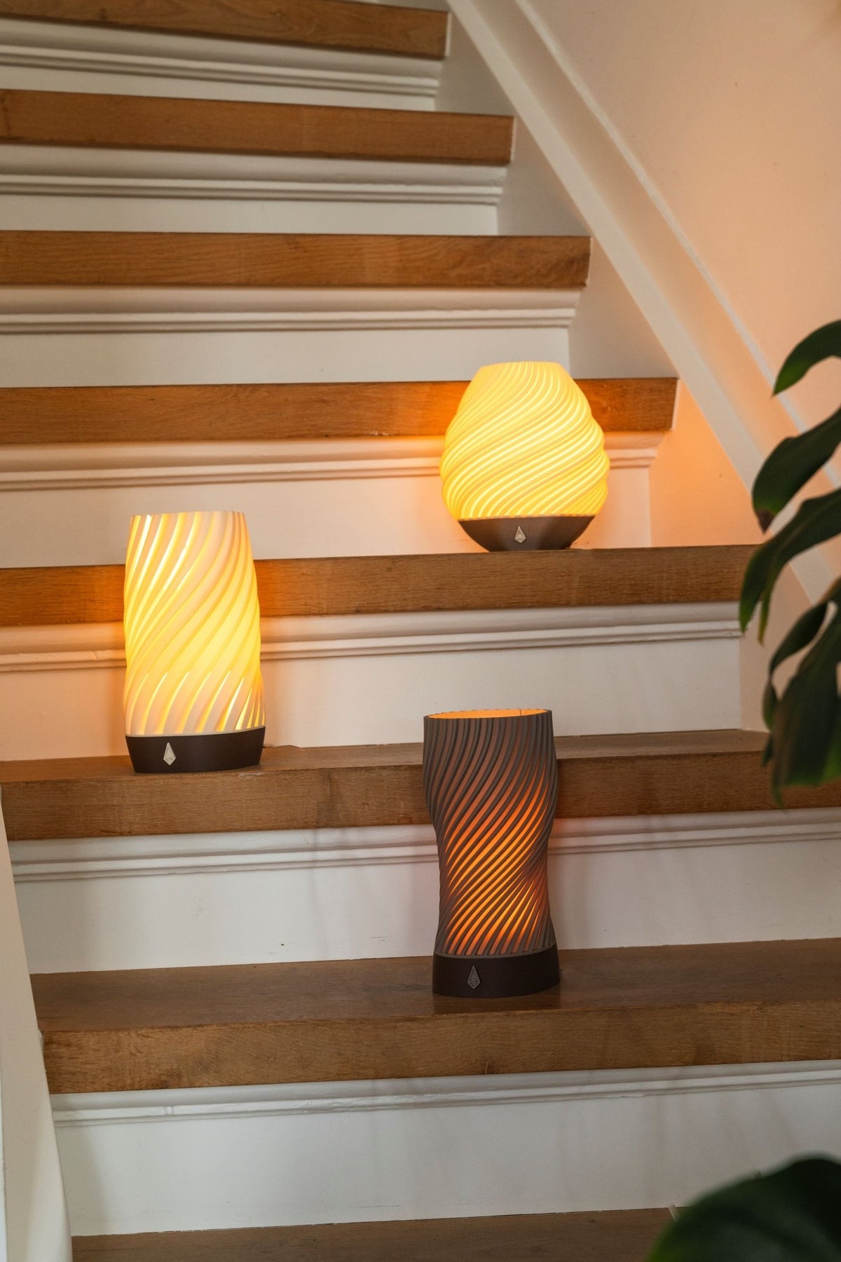 Drie brandende tafellampen in verschillende kleuren op de treden van een houten trap.
