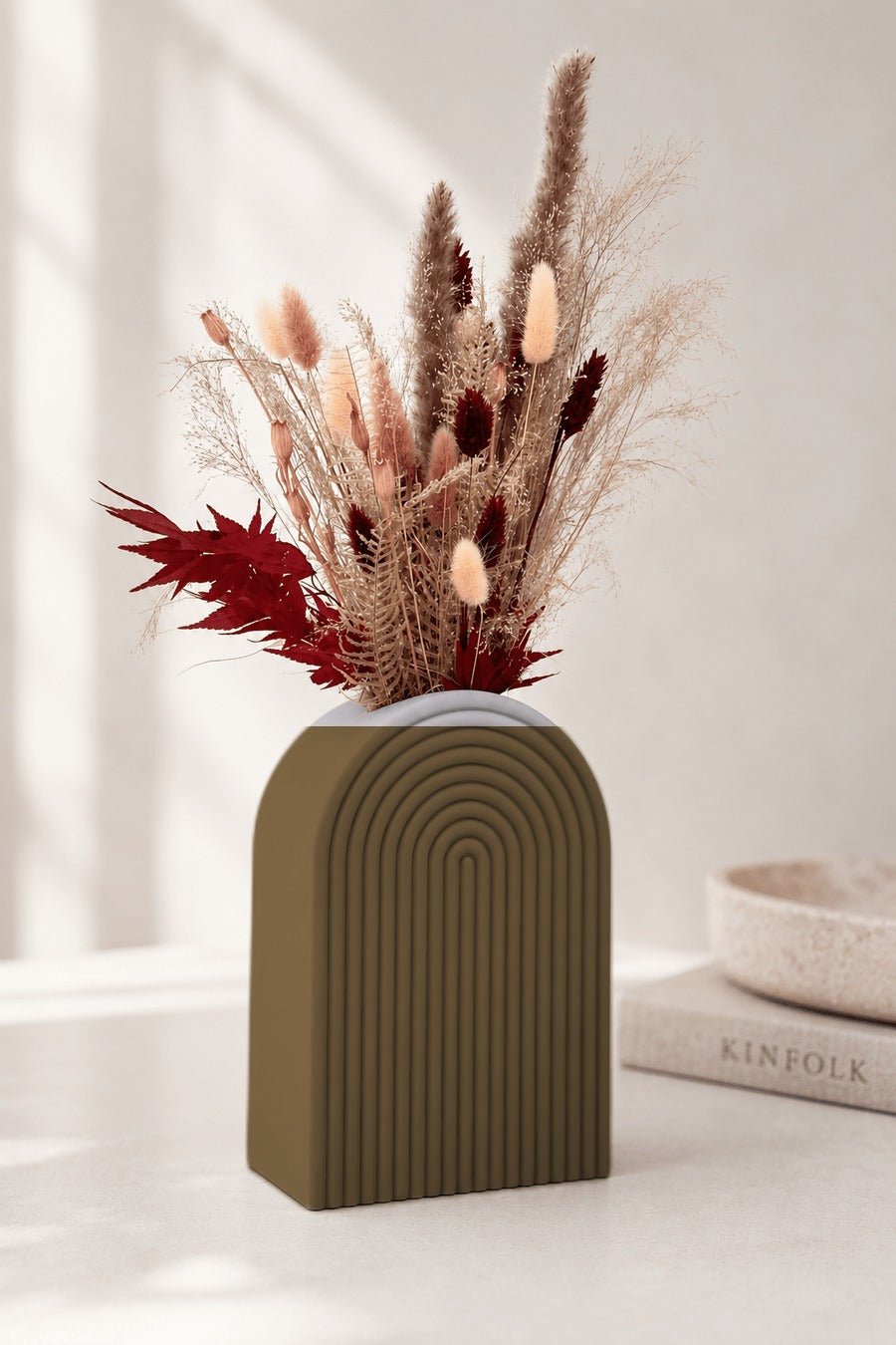 Boogvormige vaas met concentrische ribbels in goud, met droogbloemen erin.