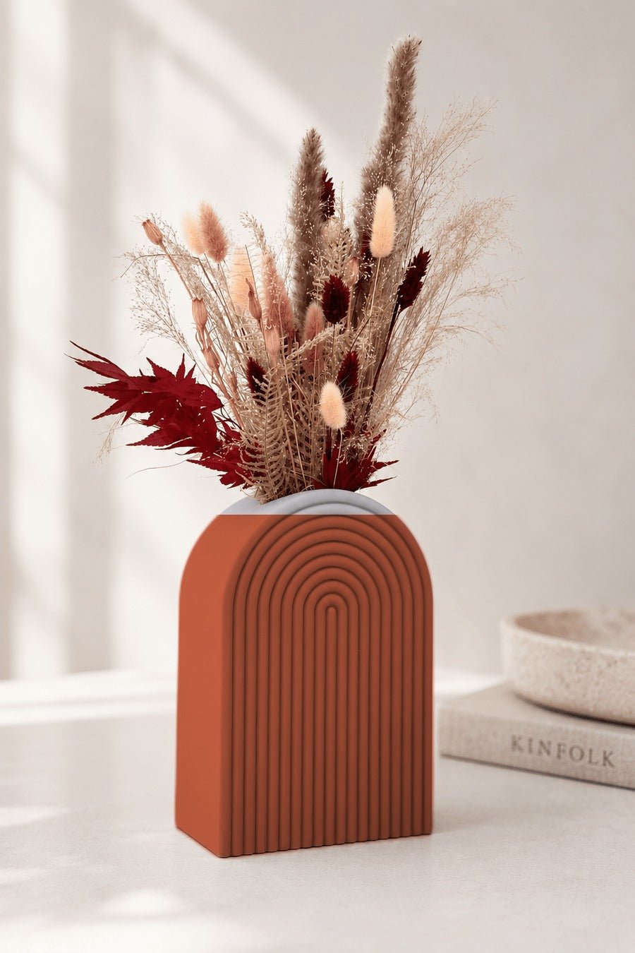 Boogvormige vaas met concentrische ribbels in terracotta, met droogbloemen erin.