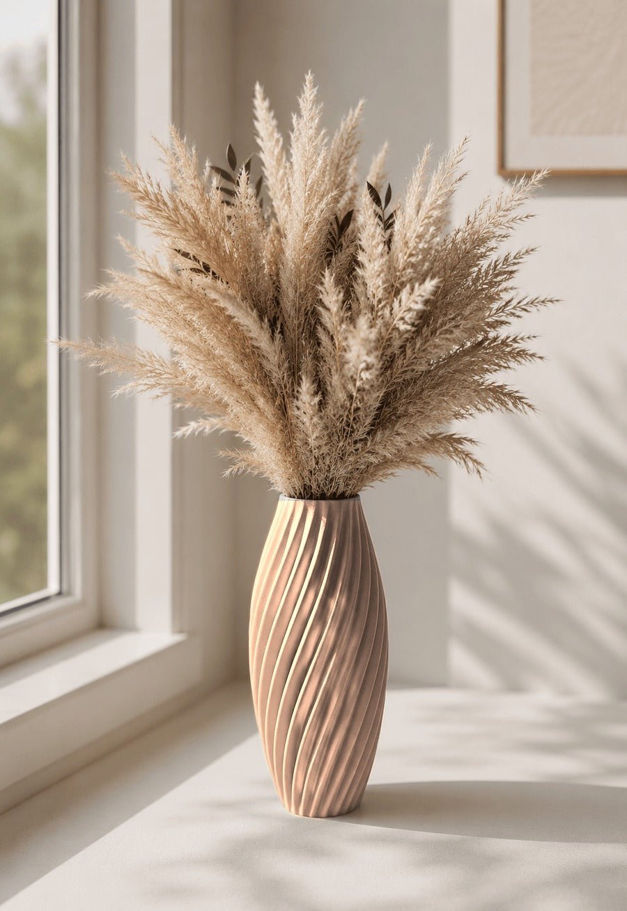 Slanke gedraaide vaas in zandbeige met pampaspluimen erin, bij een raam.