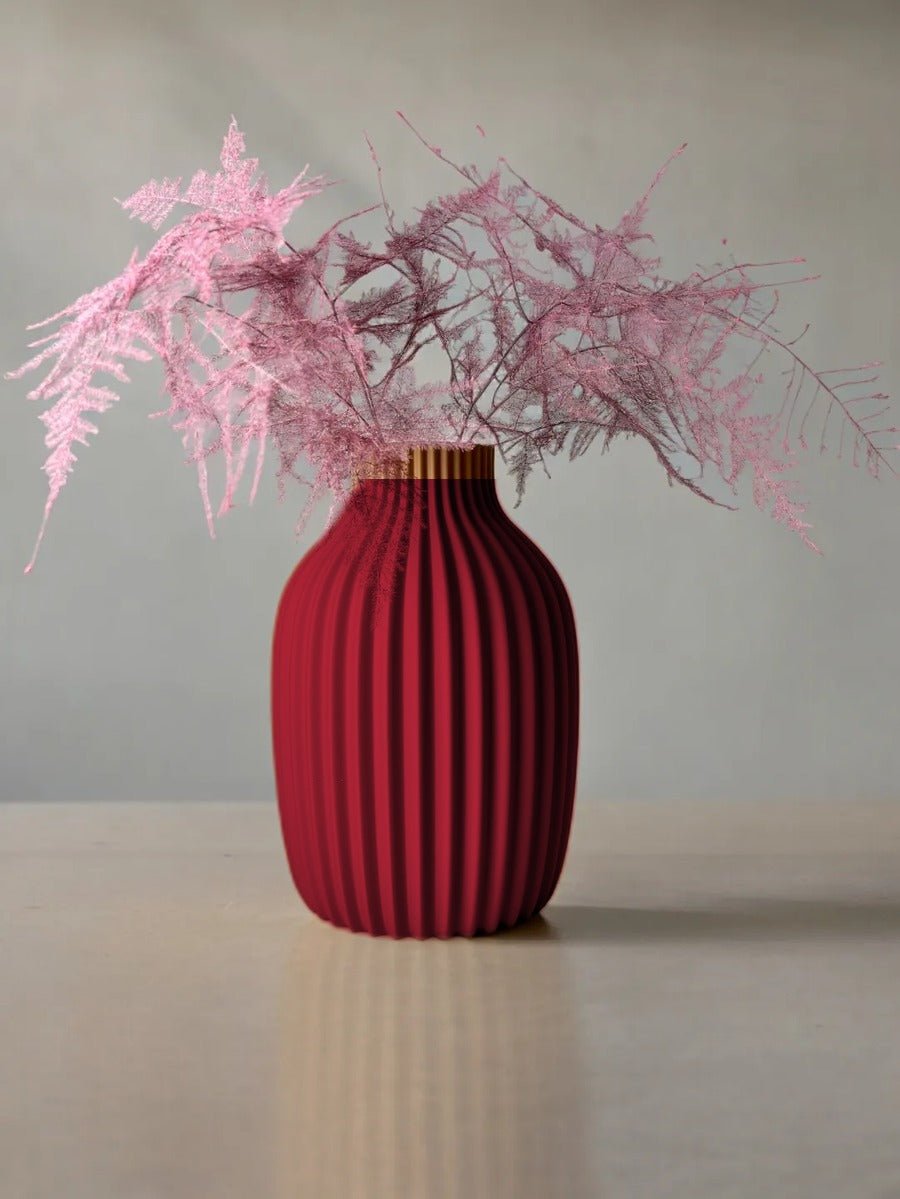 Vaas met verticale rimpelribbels in donker wijnrood, met roze droogtakken erin.