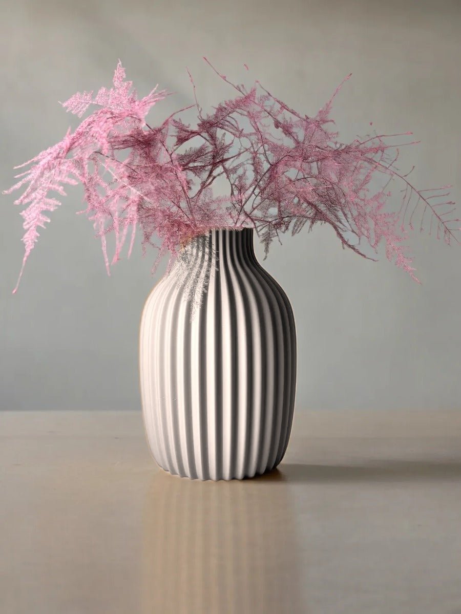 Vaas met verticale rimpelribbels in grijs, met roze droogtakken erin.
