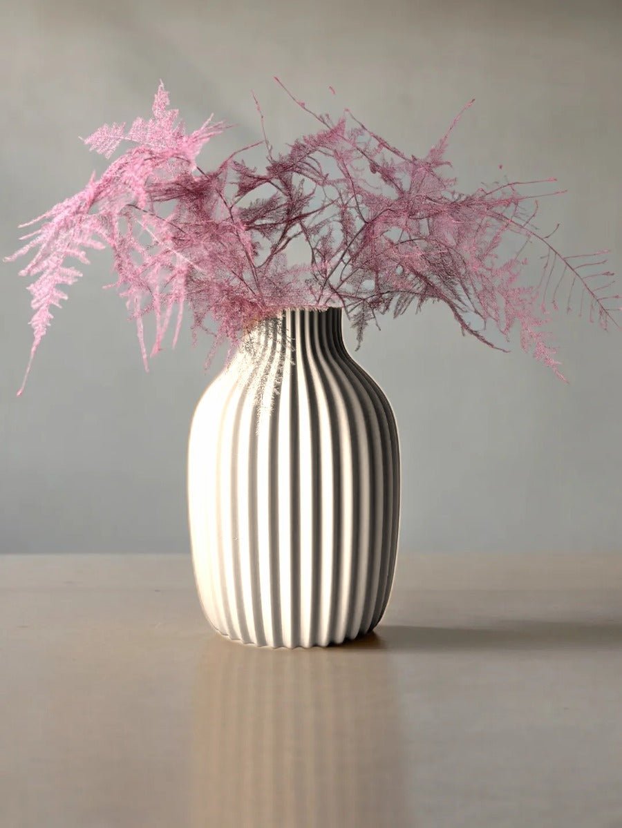 Vaas met verticale rimpelribbels in mat wit, met roze droogtakken erin.