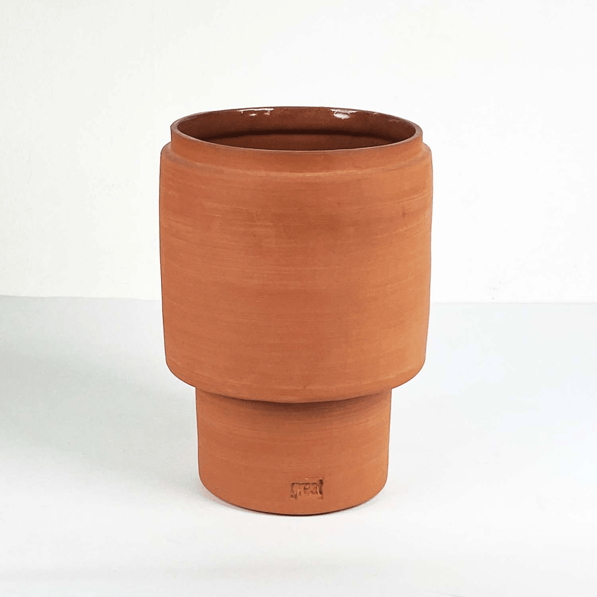 Cilindrische keramieken vaas in terracotta op een verhoogde voet.