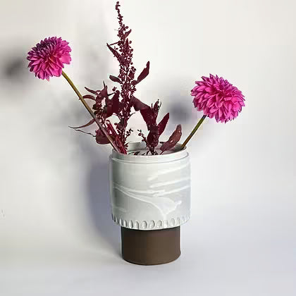 Wit geglazuurde keramieken vaas op voet met roze dahlia's en amarant.