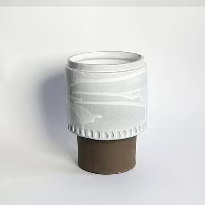 Cilindrische keramieken vaas met wit glazuur op een chocoladebruine voet.
