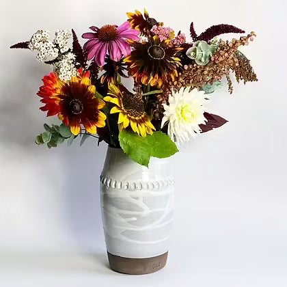 Wit geglazuurde keramieken vaas met een boeket zonnebloemen en dahlia's.