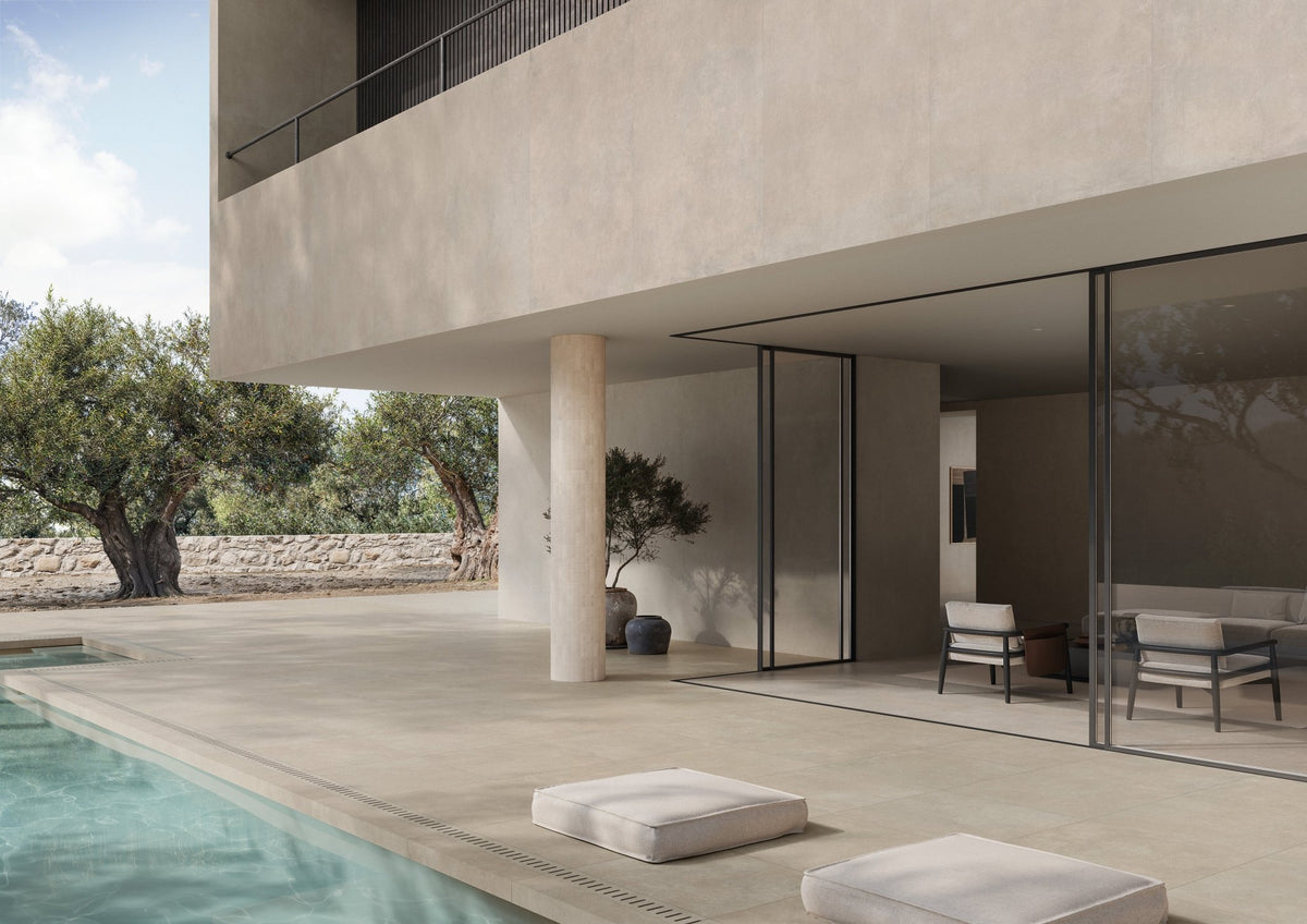 Terras met grijsbeige betonlook vloertegels langs een zwembad bij een moderne villa.